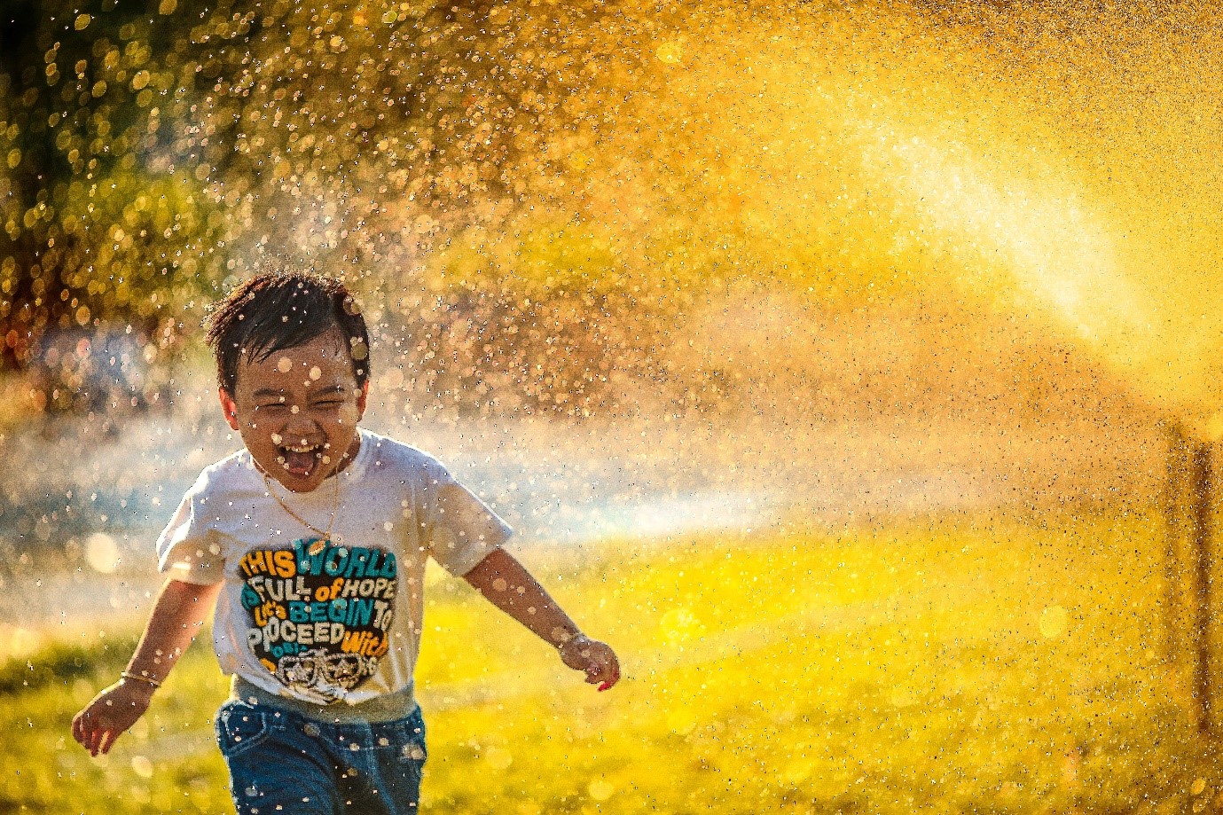 A smiling boy running through a water sprinkler. Photo by Mi Pham on Unsplash